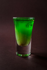 Green alcoholic shot glass with absent, irish cream, liquor on elegant dark brown background