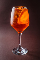 Glass of Aperol Spritz with orange on elegant dark brown background