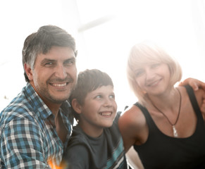 Parents and their son sit huddled in the living room and smiling