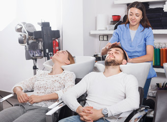 Girl  hairdresser washing hair of smiling male in salon