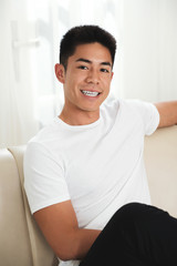 Portrait of attractive mixed-race man with white toothy smiling sitting on sofa at home
