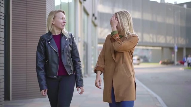 twins sisters are walking in city in warm autumn day, chatting and gossiping, charming blondes