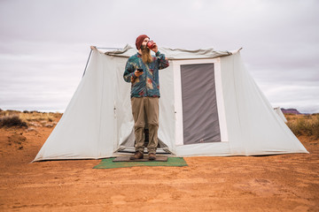 Traveler with smartphone drinking hot beverage near tent