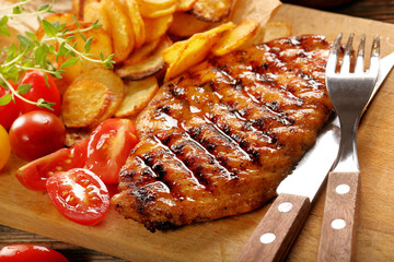Grilled chicken fillet with potato chips and fresh salad on a wooden background