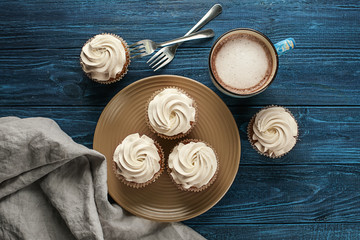 Plate with tasty cupcakes and cup of milk on wooden table