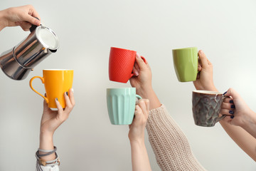 Woman pouring coffee into cups in hands of people on light background