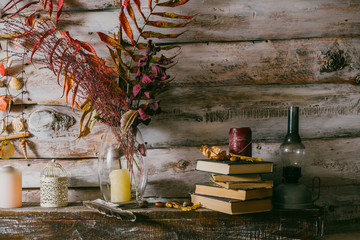 dry leaves in a vase. vintage interior. books, candle and oli lamp on the table. wooden background.autumn