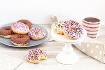 Delicious glazed donuts and cup of coffee on light wooden background