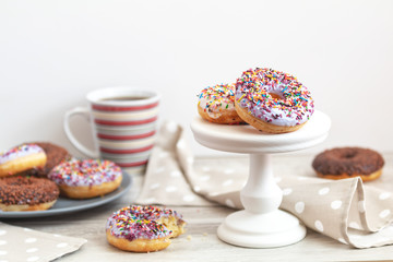 Delicious glazed donuts and cup of coffee on light wooden background