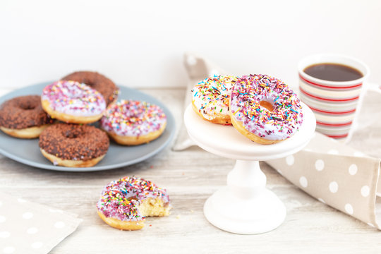 Delicious glazed donuts and cup of coffee on light wooden background