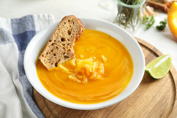 Plate with tasty pumpkin cream soup on wooden board
