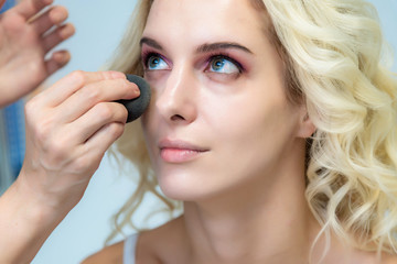 The work of a professional make-up artist, beautician, makes makeup on the face of a blonde girl with shadows on the eyes.
