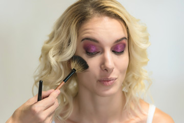 Obraz premium The work of a professional make-up artist, beautician, makes makeup on the face of a blonde girl with shadows on the eyes.