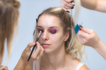 Fototapeta premium The work of a professional make-up artist, beautician, makes makeup on the face of a blonde girl with shadows on the eyes.