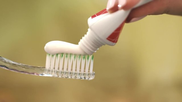Woman hand holding toothbrush and tooth paste tube. Close up of white toothpaste squeezing on toothbrush. Morning teeth brushing. Oral hygiene and caries prevention