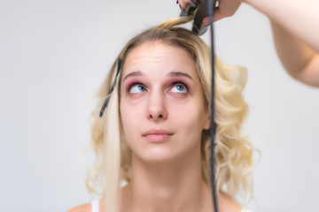 Fototapeta premium The work of a professional makeup artist - hairdresser, makes the hair style of a beautiful blonde girl.