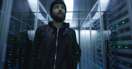 Medium shot of a two hackers walking through corporate data center with rows of working rack servers
