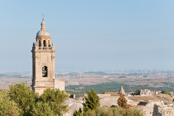 Fototapeta na wymiar Bell along with ruins of a roofless church, the background is a rural landscape with windmills, is located in the town of Medina Sidonia in Spain. 