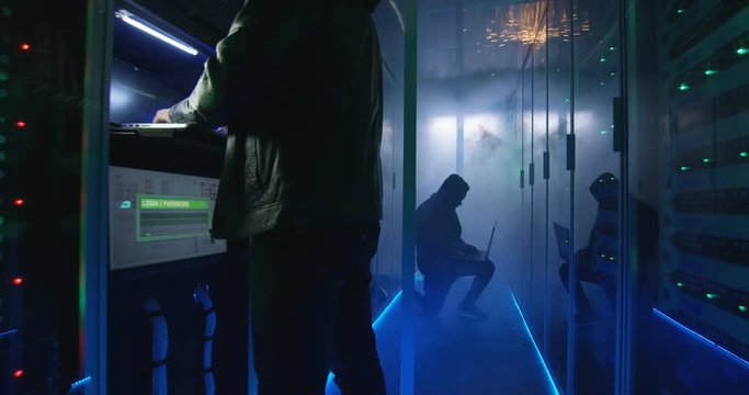 Medium, slow motion shot of a two hackers finishing hack and escaping a spark and smoke-filled corporate data center
