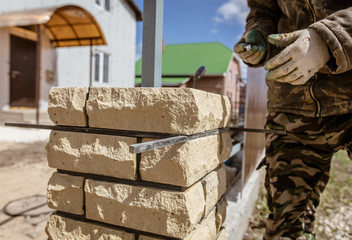 The worker is laying bricks on the fence