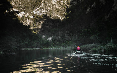 A lone kayaker paddling down a remote river with the sunset reflecting of the calm water