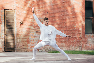 handsome young man in white clothes dancing on urban street