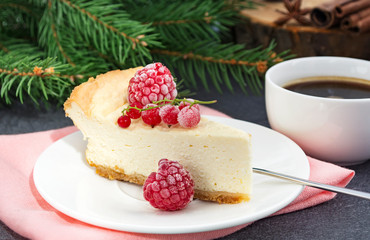 Cheesecake, decorated frozen red currant berries, and coffee cup on pine tree branch background. Christmas dessert with summer taste