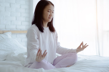 Obraz na płótnie Canvas Asian girls sitting on yoga poses in bed in a warm morning.Yoga on the bed at dawn Good for the body and the mind.Warm tone.Do not focus on objects.