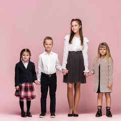 Cute smiling happy stylish children on pink background. Beautiful stylish teen girls and boy standing together and posing at studio. Classic style. Kids fashion and emotions concept.