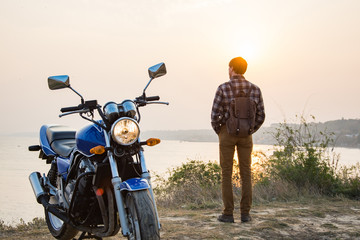 Young male traveler with motorbike against beautiful sunset