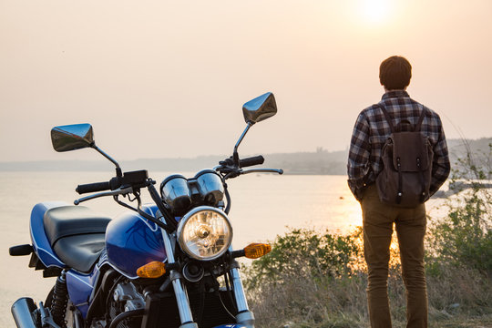 Young male traveler with motorbike against beautiful sunset