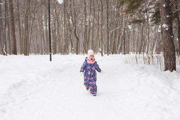 Fototapeta na wymiar Winter, childhood and nature concept - baby girl walking in the winter outdoors