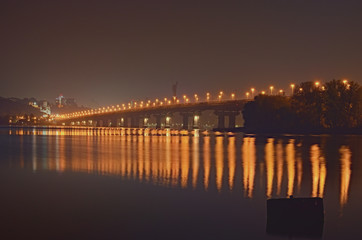 Fototapeta na wymiar Autumn night cityscape with Paton bridge over Dnieper river. Motherland monument at the background. City lights reflected in the water. Kyiv, Ukraine