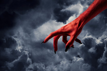 Halloween red devil monster hand with black fingernails against a dark sky