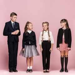 Cute smiling happy stylish children on pink background. Beautiful stylish teen girls and boy standing together and posing at studio. Classic style. Kids fashion and emotions concept.