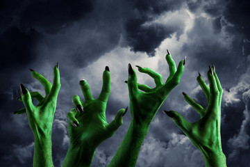Halloween green monster hand with black fingernails against a dark sky