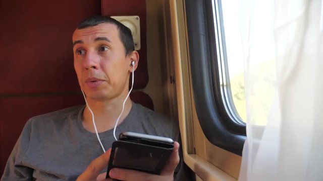 man listening to the music on the train rail car coupe compartment travel. slow motion video. man with a smartphone at the window lifestyle of a train in a car travel internet social media web. man
