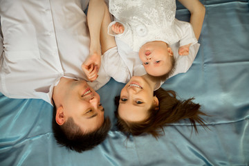 beautiful young family mom and dad lie on the bed with the little daughter at home
