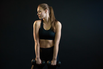 Fototapeta na wymiar beautiful young girl goes in for sports with dumbbells on a black background