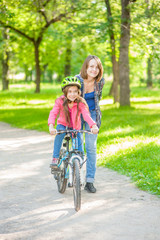 Happy family. Smiling mom teaches her daughter to ride a bicycle in the park