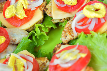 Bbq meat with cheese, tomatoes, onions and lettuce. On a roll and green plastic board