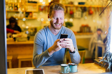 Fototapeta na wymiar Handsome man using mobile phone in coffee shop