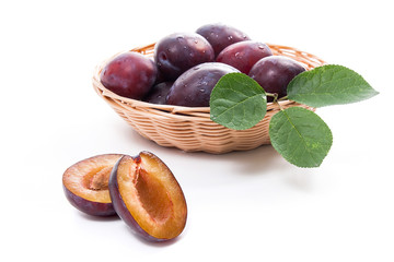 Yellow wooden basket with ripe plums, whole and half ripe plums isolated on a white background..
