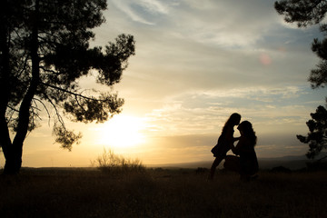 Fototapeta na wymiar backlight of a mother kissing her daughter in a pine forest with yellow sky at sunset sunrise