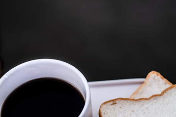 White bread and glass placed on the table in the morning.On the breakfast table there was a glass of coffee and a plate of bread.Breakfast set on wooden floor in the morning.