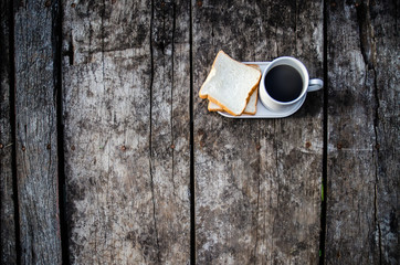 Black coffee and bread plate on wooden table.White bread and glass placed on the table in the morning.On the breakfast table there was a glass of coffee and a plate of bread.