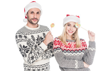 portrait of young caucasian couple in santa claus hats with lollipops isolated on white