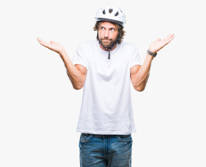 Handsome hispanic cyclist man wearing safety helmet over isolated background clueless and confused expression with arms and hands raised. Doubt concept.