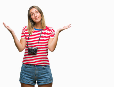 Young beautiful woman taking pictures using vintage photo camera over isolated background clueless and confused expression with arms and hands raised. Doubt concept.
