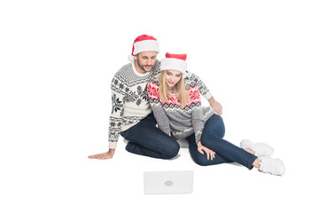 young couple in sweaters and santa claus hats with laptop isolated on white